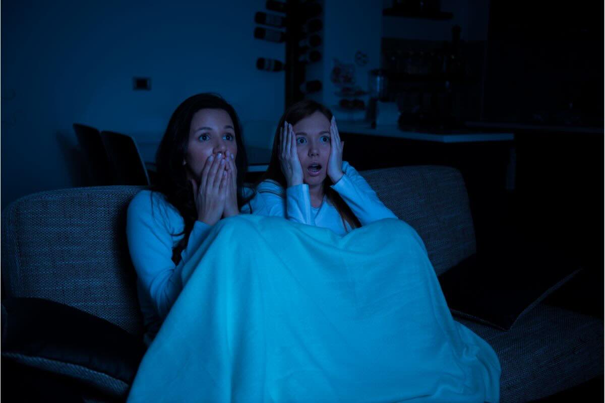 Sotto le coperte due donne spaventate guardano qualcosa in tv