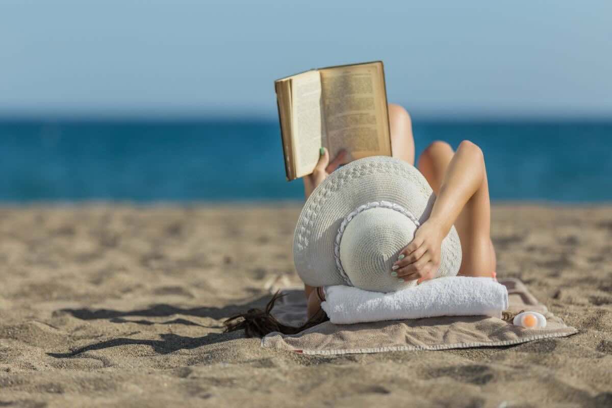 Donna sdraiata sulla sabbia legge libro