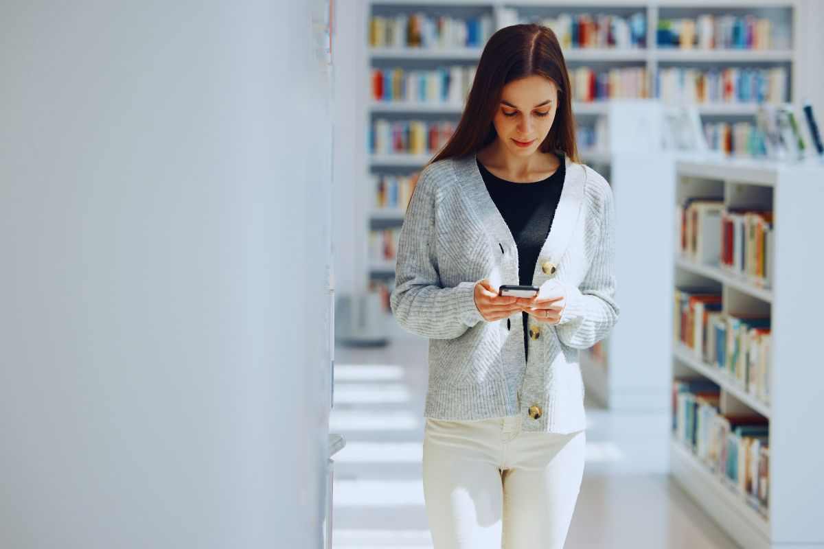 Ragazza che legge messaggi su smartphone in biblioteca