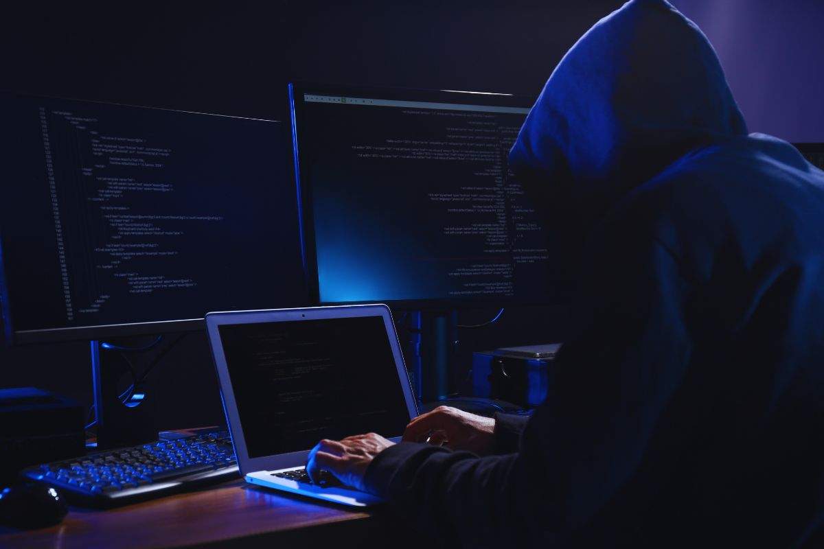 Uomo incappucciato che utilizza vari computer per scrivere codici