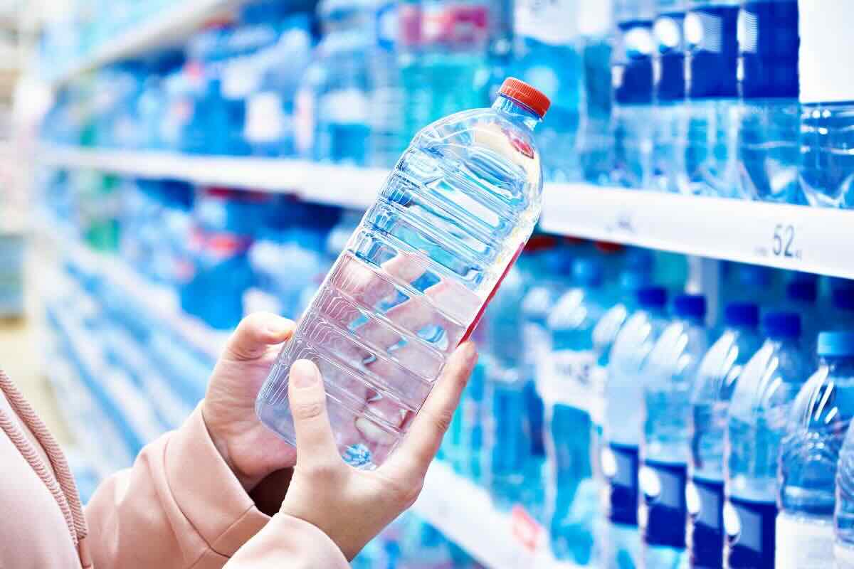 Mani con bottiglia di acqua al supermercato, legge etichetta