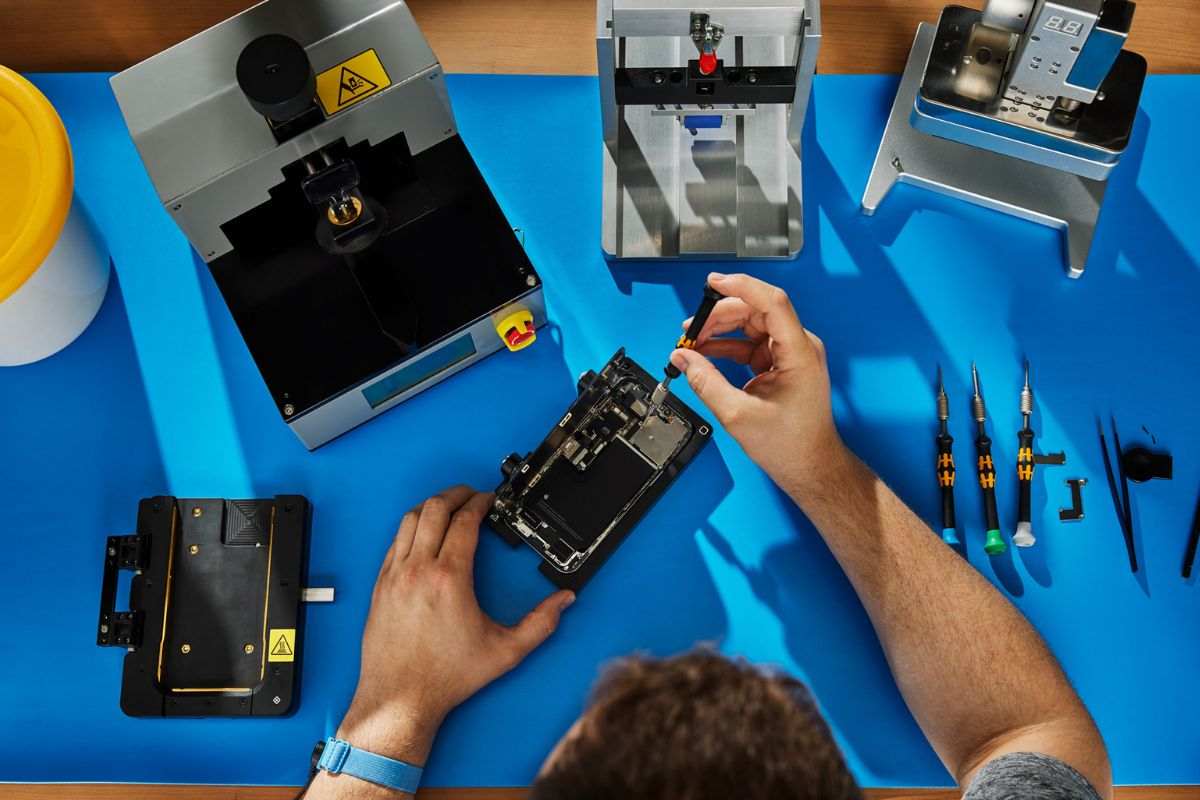 uomo al banco da lavoro che ripara iPhone con cacciavite