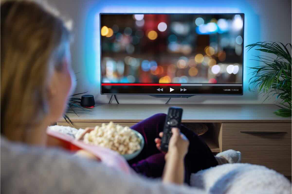 Donna seduta sul divano con telecomando e pop corn guarda tv