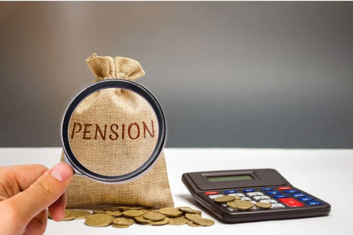 Lente di ingrandimento inquadra parola "Pension" su sacco, monete, calcolatrice