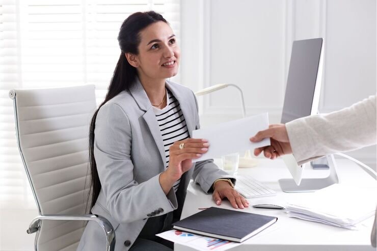 Ragazza seduta alla scrivania prende busta comunicazione da un'altra mano