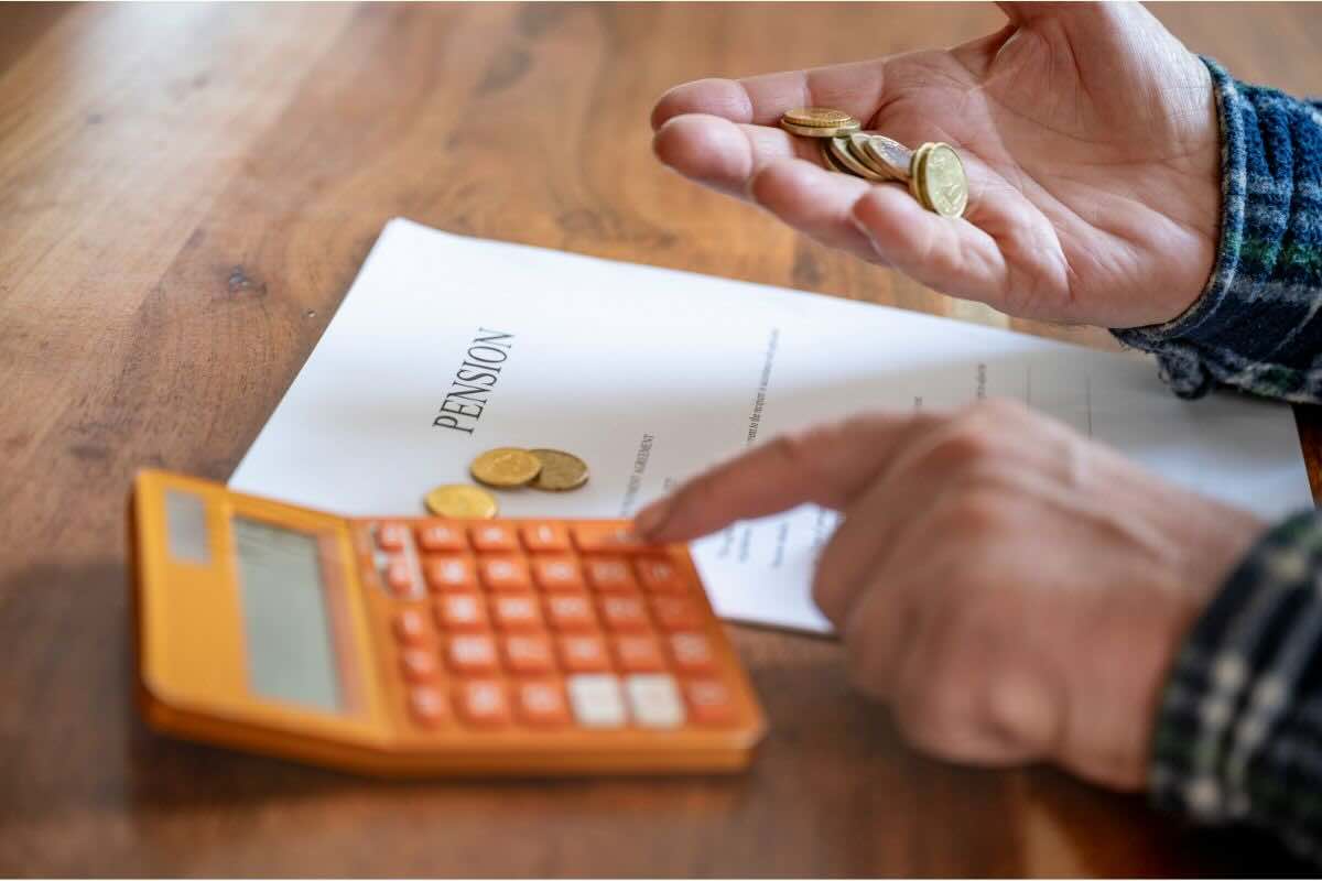Mano con monete, calcolatrice, documento con scritto "pension"