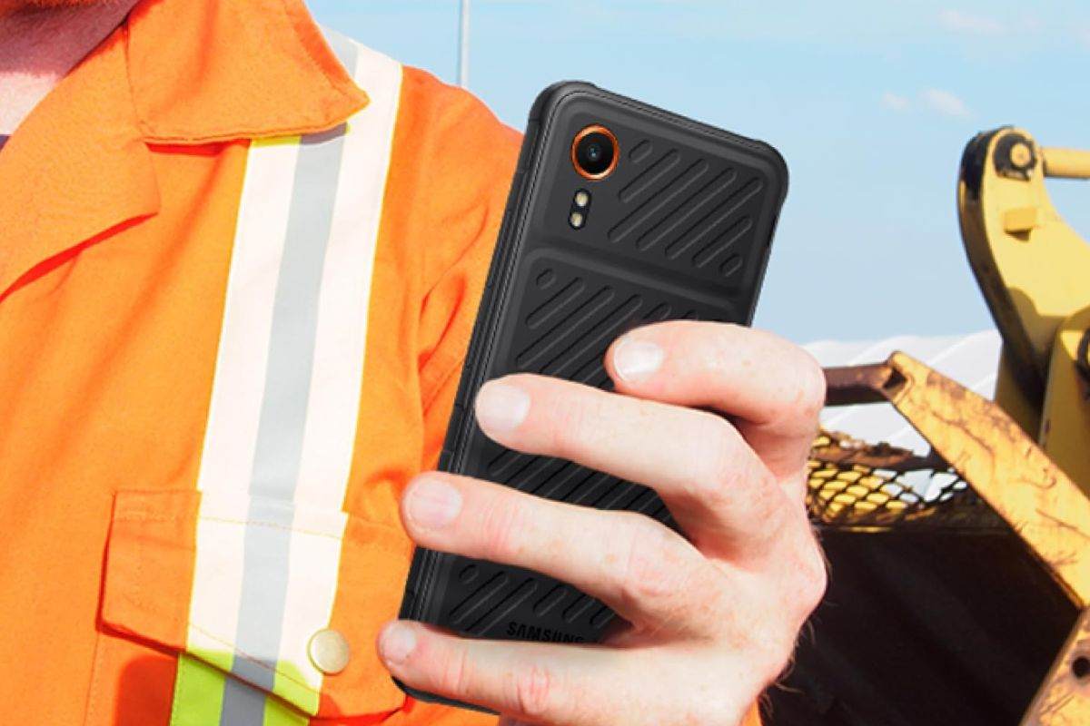 Samsung Galaxy XCover7 tenuto in mano da persona con camicia arancione