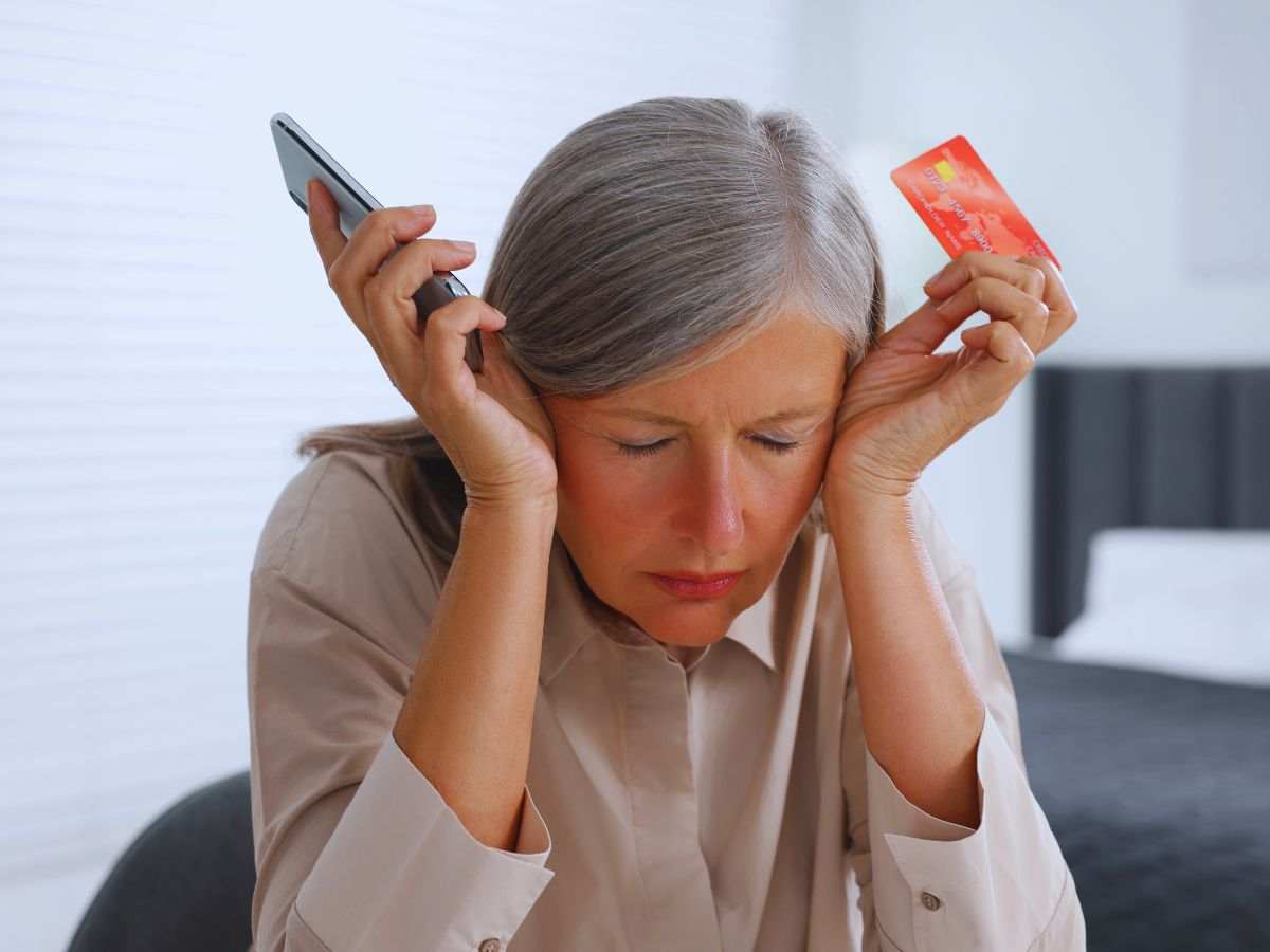 signora che si mette le mani nei capelli disperata con telefono e carta di credito nelle mani