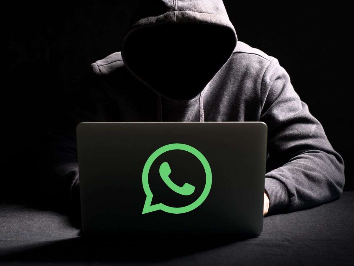 Uomo incappucciato nell'oscurità che usa un PC con logo WhatsApp sopra