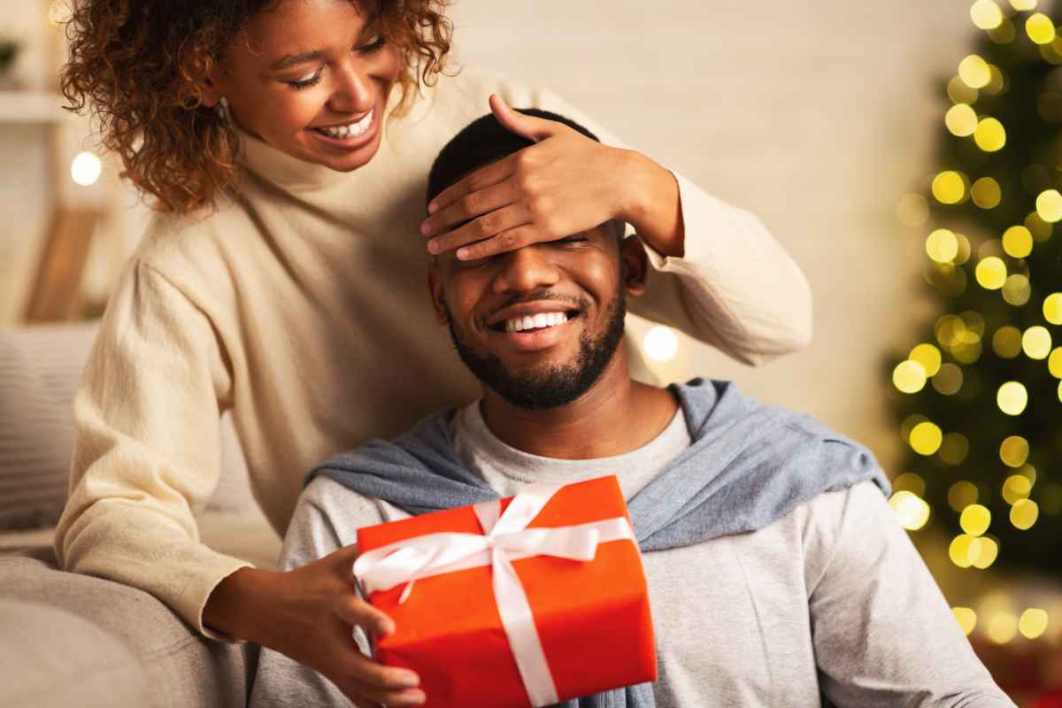 una ragazza copre gli occhi al fidanzato nel consegnarli il regalo di Natale